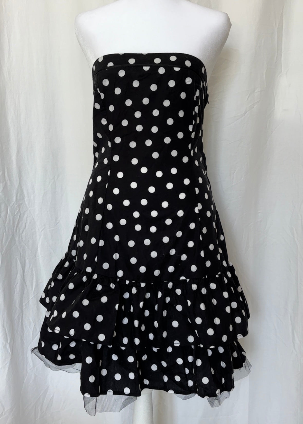 Black strapless dress with white polka dots on a mannequin against a white background